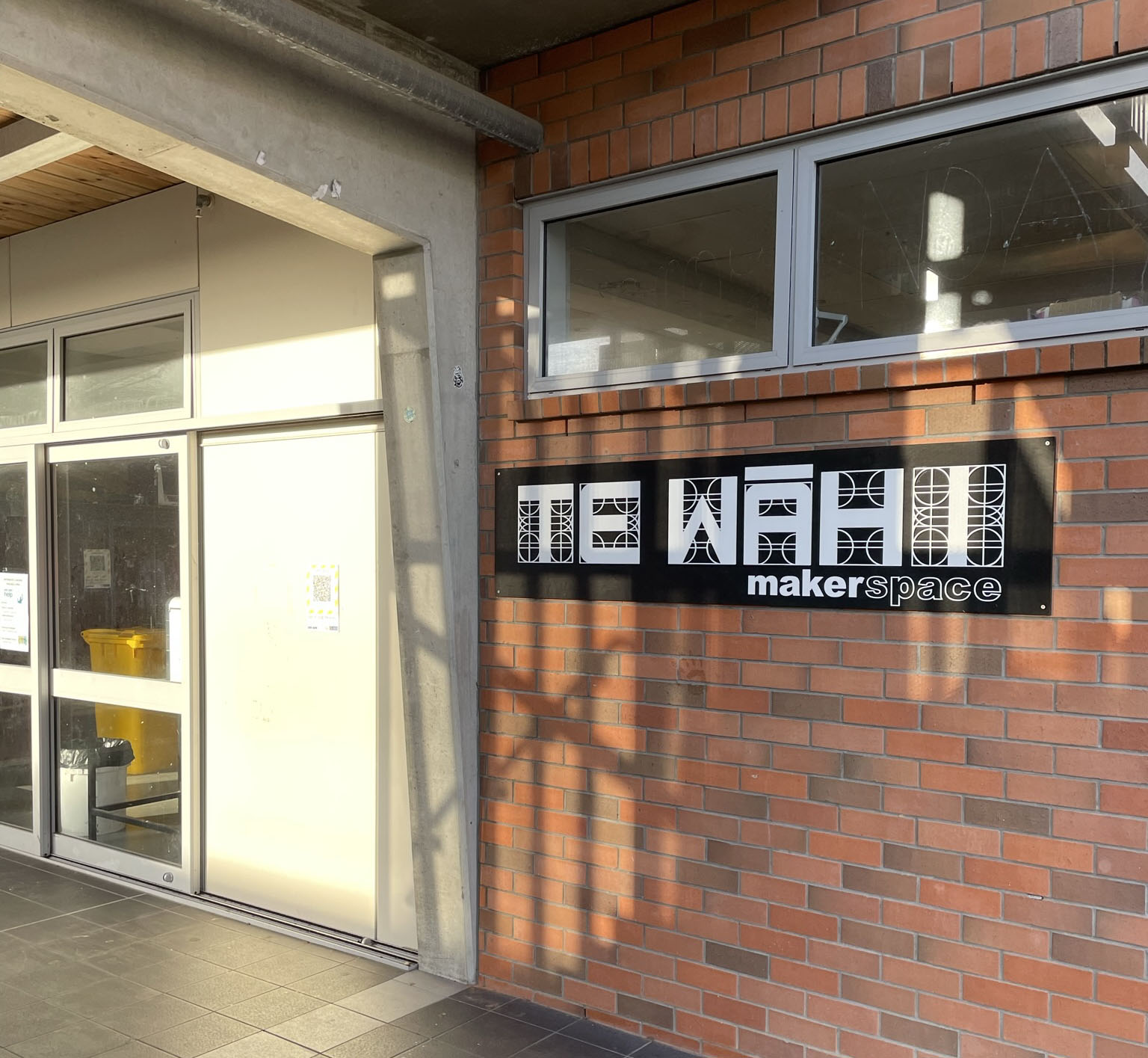 Entrance of the Te Wāhi maker space, showing a monochrome sign on a brick wall.